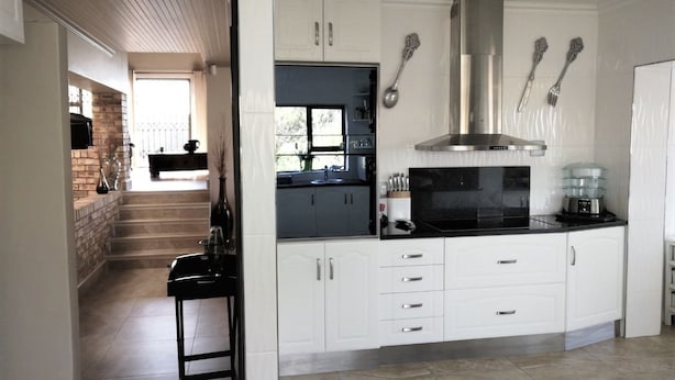 A modern kitchen with white cabinets, a stainless steel range hood, and a black countertop. - Coastal Haven 4 (Gqeberha (Port Elizabeth))