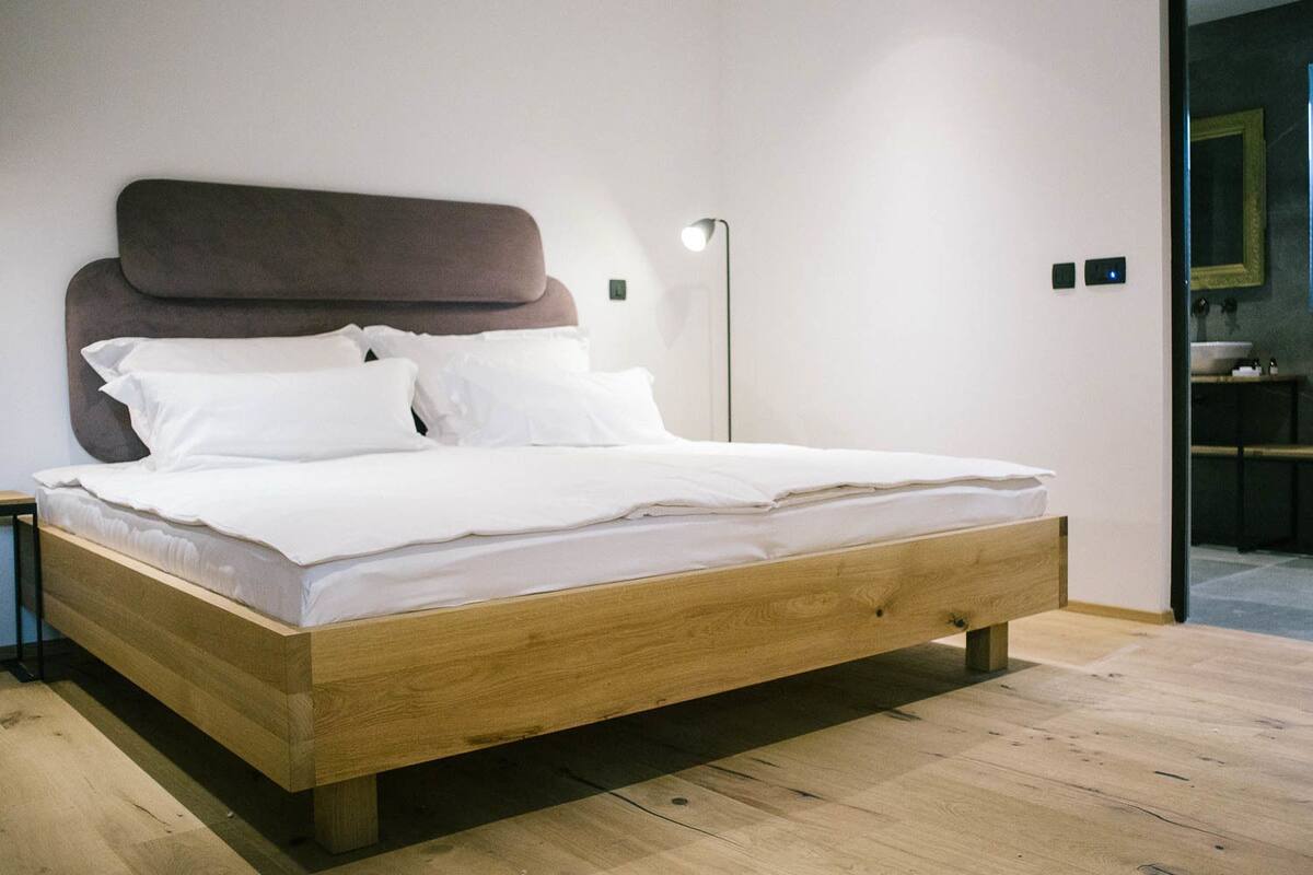 A modern bedroom with a wooden bed frame, white bedding, and a large headboard.