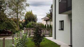 Ein modernes Gebäude mit weißer Fassade, ein kleiner Baum im Vorgarten und ein Zaun.