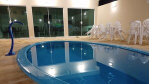 A swimming pool with a blue interior, surrounded by a wooden deck and glass doors. - Pousada Ubarana (Maragogi)