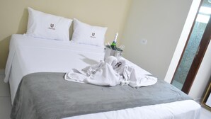 A hotel room with a bed, a grey blanket, a bottle of champagne, and a towel on the bed. - Pousada Ubarana (Maragogi)