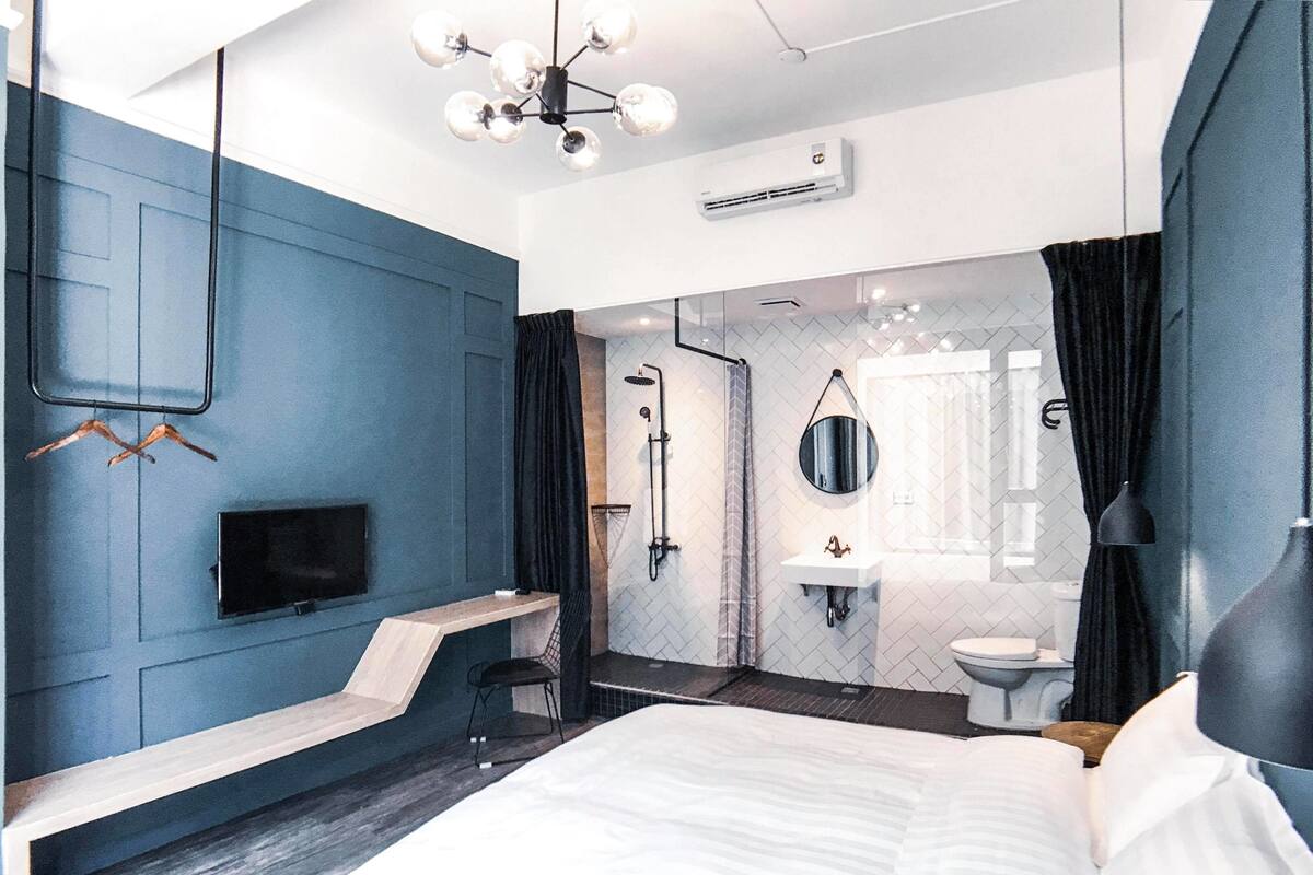 A modern hotel room with a large bed, a TV, a desk, and a shower area.