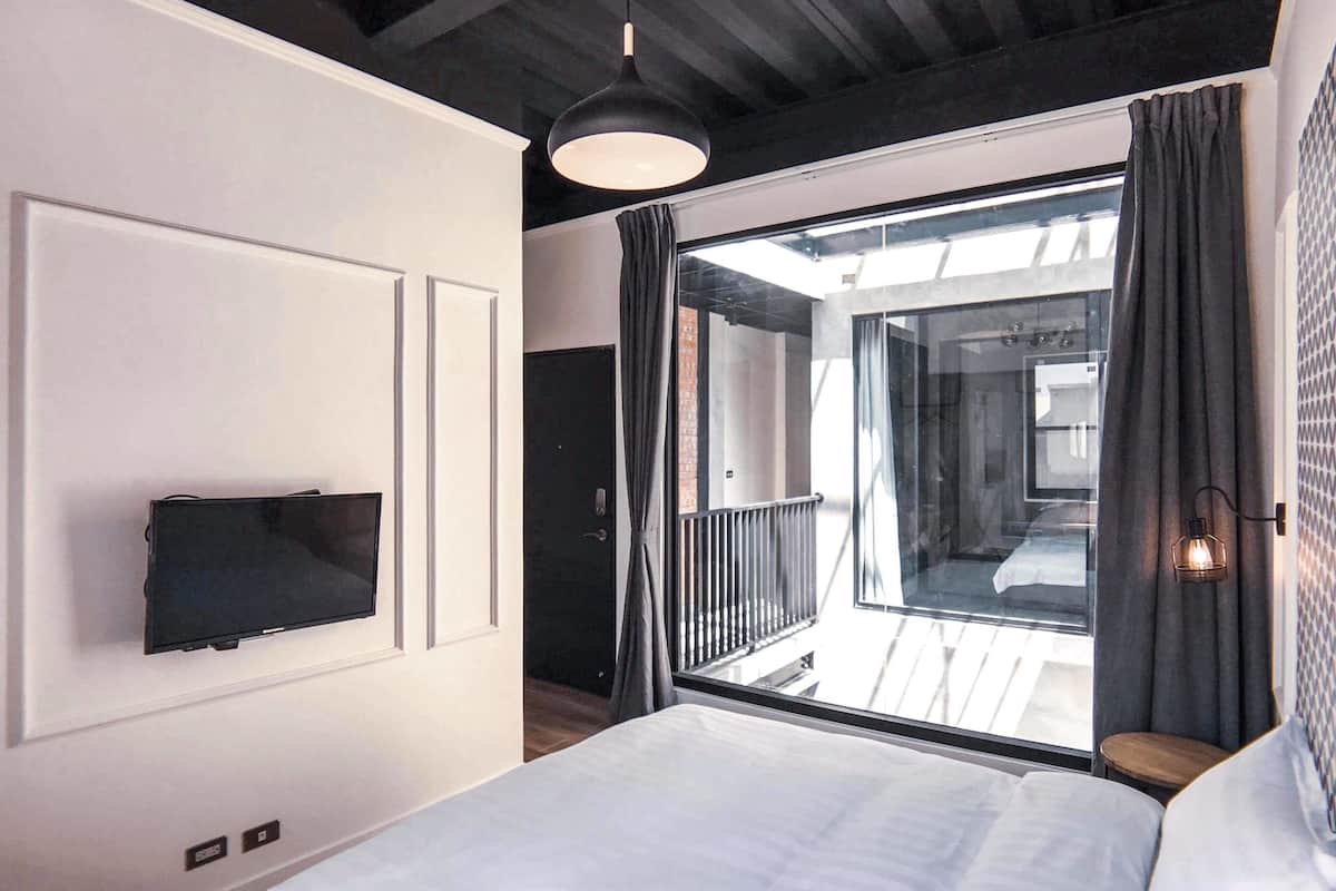 A bedroom with a bed, a TV mounted on the wall, a balcony with a view, and a hanging light fixture.