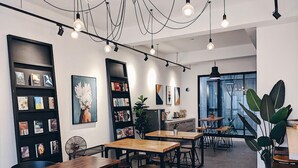 A modern cafe with wooden tables and chairs, bookshelves, and artwork on the walls. - The Gatsby Apartment (Tainan)