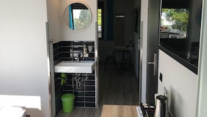 A modern bathroom with a white sink, black tiles, a green trash bin, and a mirror. - Xotel (Xanten)