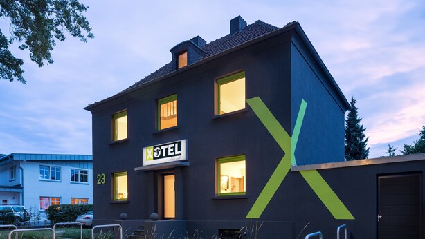 A modern hotel with a dark facade, multiple windows, and a prominent 'X' logo. - Xotel (Xanten)