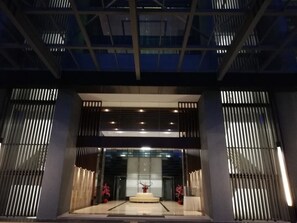 Une entrée moderne avec une façade en verre, un podium central blanc et des stores verticaux de chaque côté.