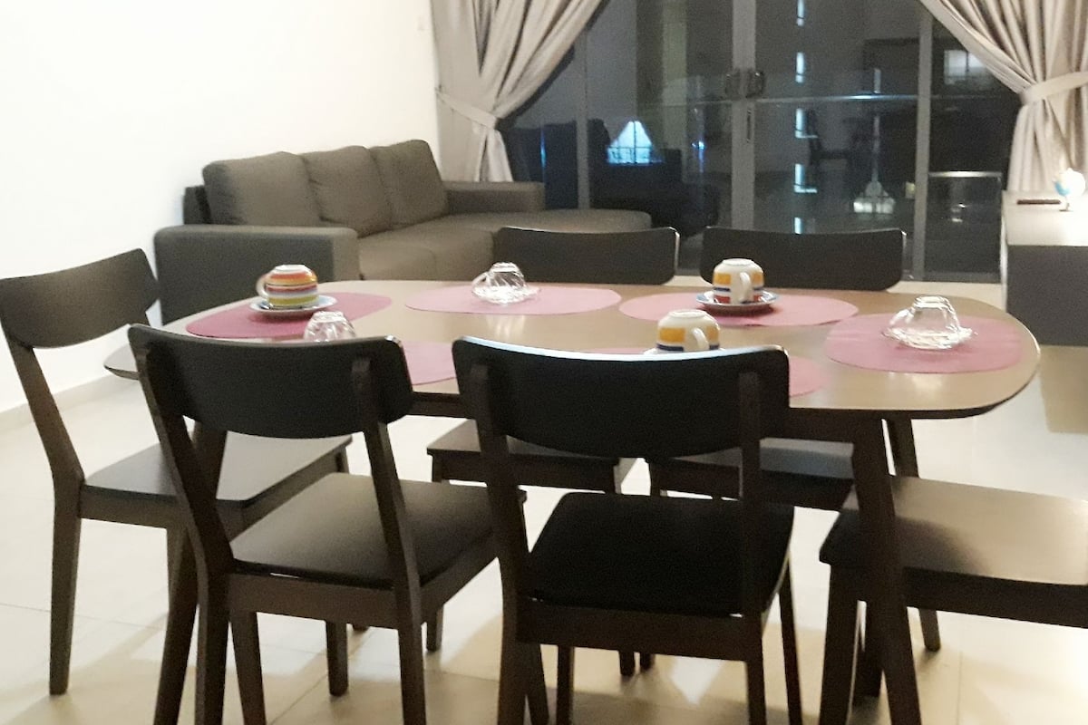 A dining area with a round table, four chairs, and a sofa in the background.