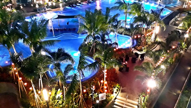 Ein großer Außenpool, umgeben von Palmen und Liegestühlen, mit einer Treppe, die zum Pool führt.