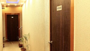 Ένας στενός διάδρομος με δύο πόρτες, η μία με την επιγραφή «ΧΩΡΟΣ ΗΛΕΚΤΡΙΚΩΝ ΕΓΚΑΤΑΣΤΑΣΕΩΝ» και η άλλη με έναν αριθμό. Κατά μήκος του διαδρόμου υπάρχουν γλάστρες με φυτά.
