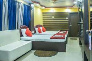 A hotel room with a sofa, two beds, a ceiling fan, and a door.