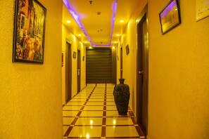 A hotel hallway with a checkered floor, a large vase, and framed artwork on the walls. - OYO 1622 Hotel Balaji International (Barakpur)