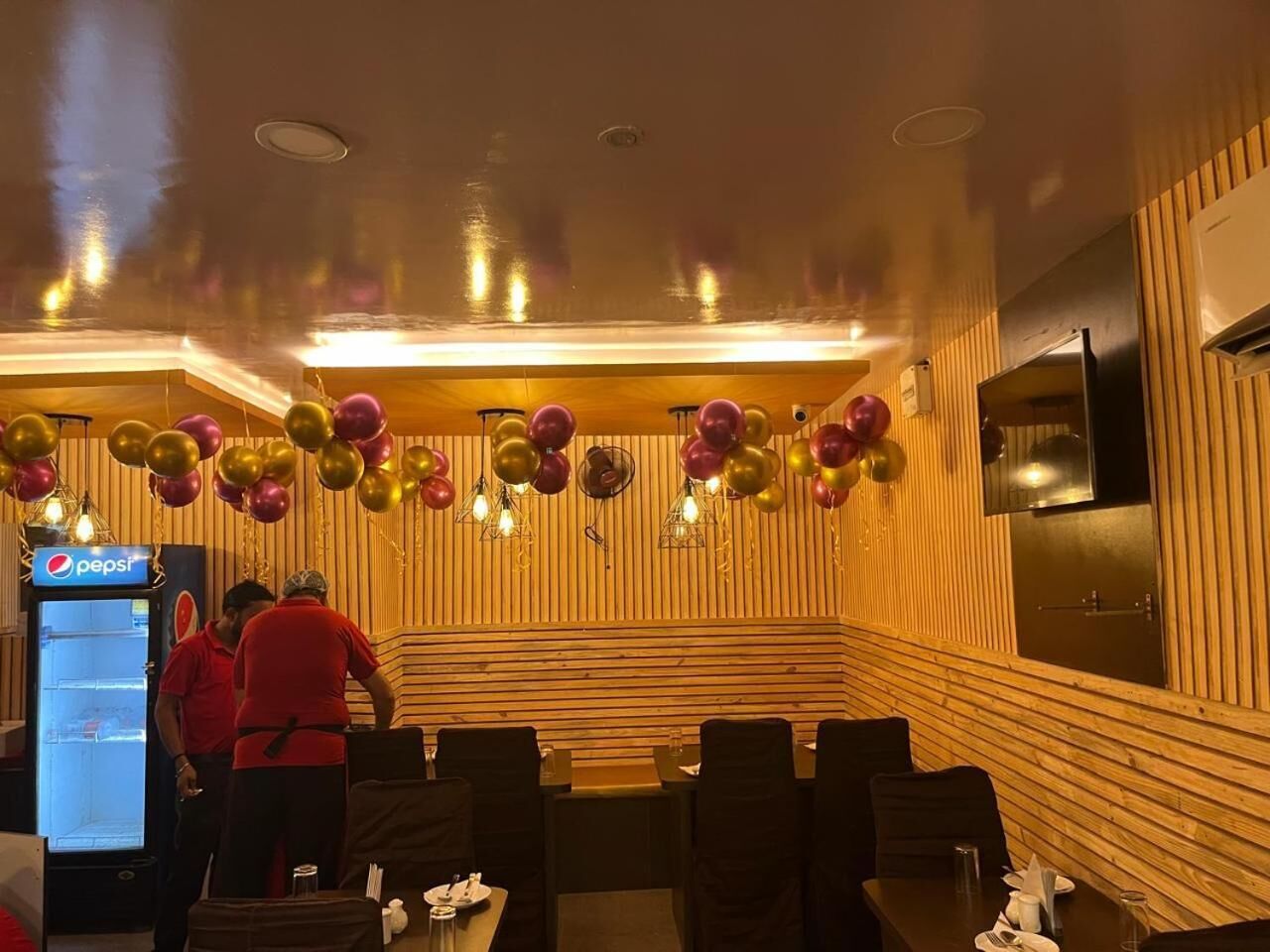 A restaurant with wooden paneling, a pepsi refrigerator, and balloons.