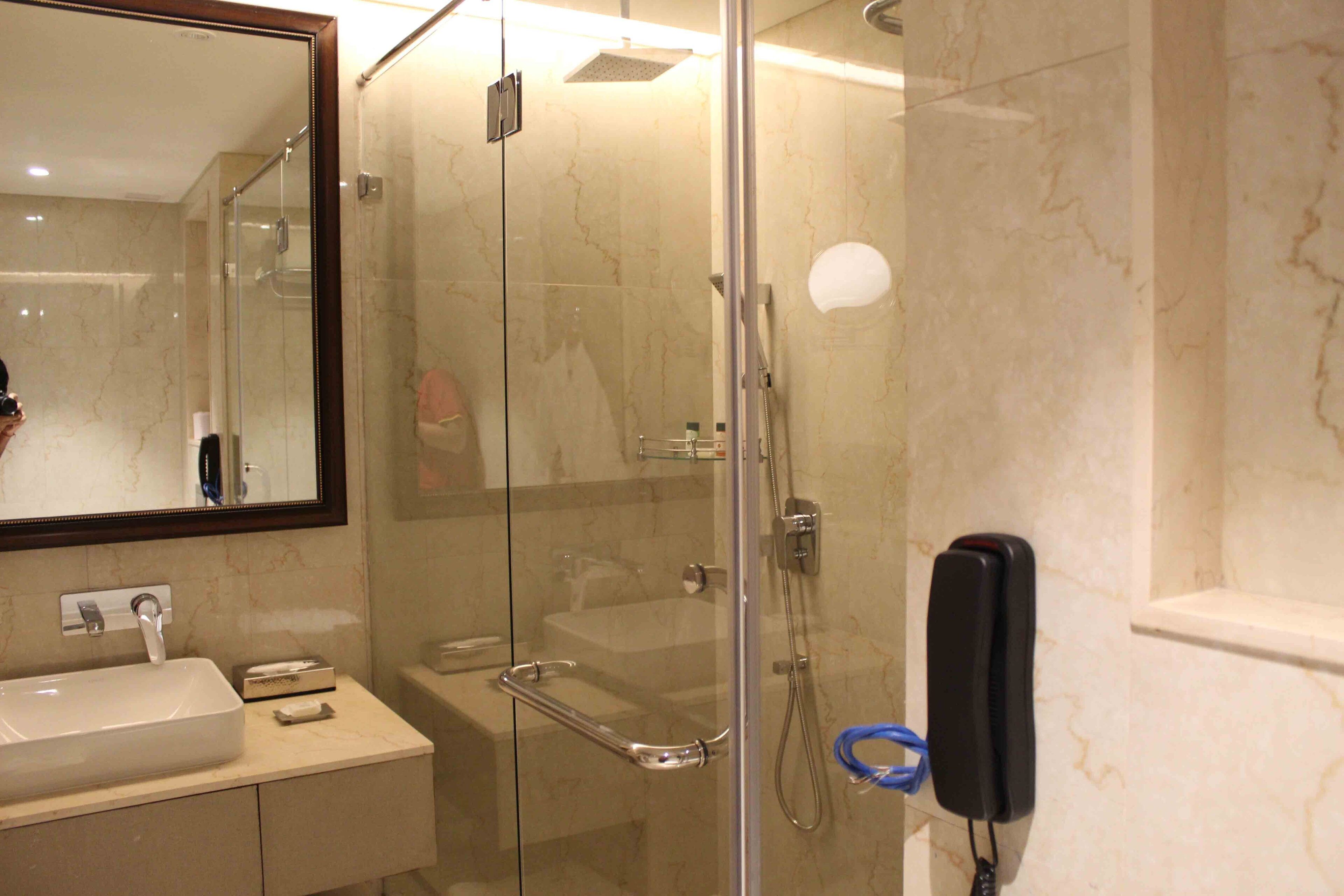 Een moderne badkamer met een douchecabine van glas, een wastafel met spiegel en een handdouche.
