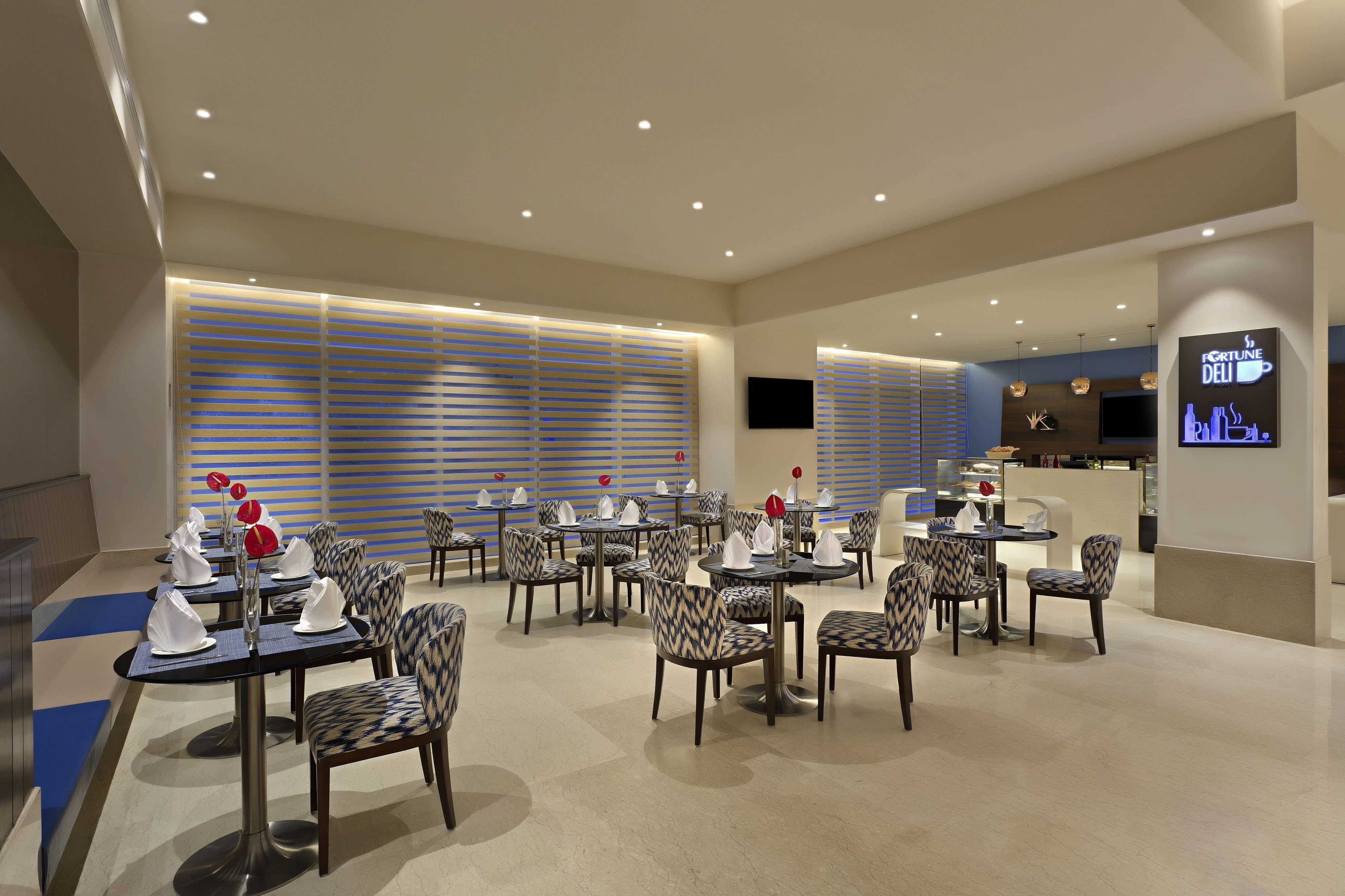 A modern dining area with multiple tables and chairs, a bar area, and a television screen.