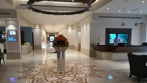 En hotellobby med en receptionsdisk, en stor blomsterdekoration och en modern takdesign.