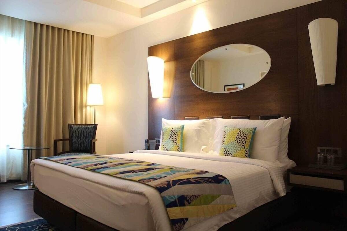 Une chambre d’hôtel avec un grand lit, un miroir rond, une chaise et une table de chevet.
