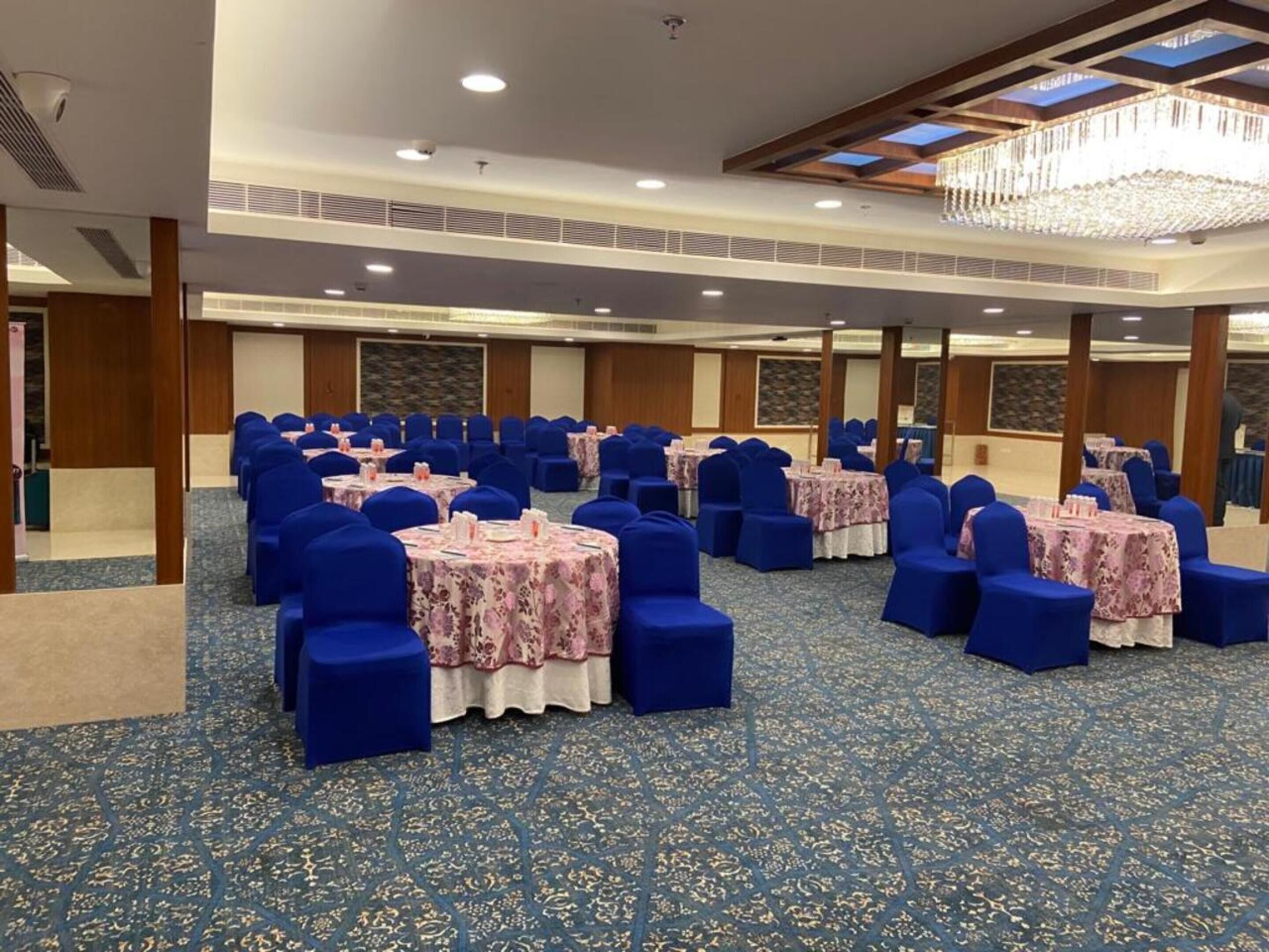A conference room with rows of blue chairs and tables, a patterned carpet, and a chandelier.