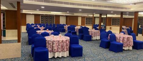 A conference room with rows of blue chairs and tables, a patterned carpet, and a chandelier.