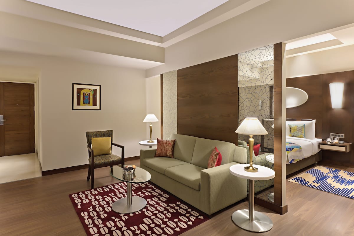 Une chambre d’hôtel comprenant un canapé, un fauteuil, une table de chevet, une lampe et un lit avec un tapis à motifs.