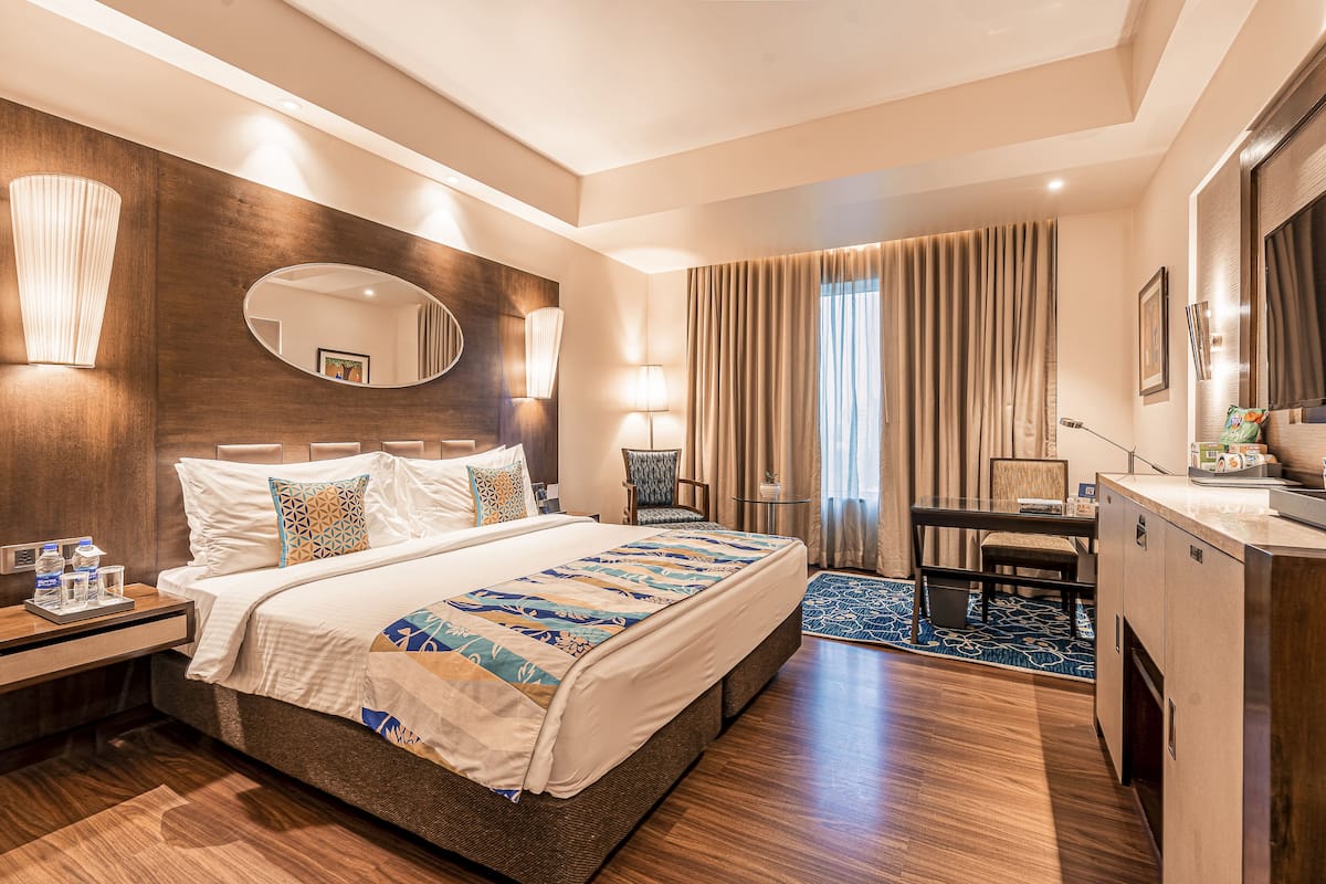 Une chambre d’hôtel avec un grand lit, un bureau, une chaise, un miroir et une petite table avec une lampe.