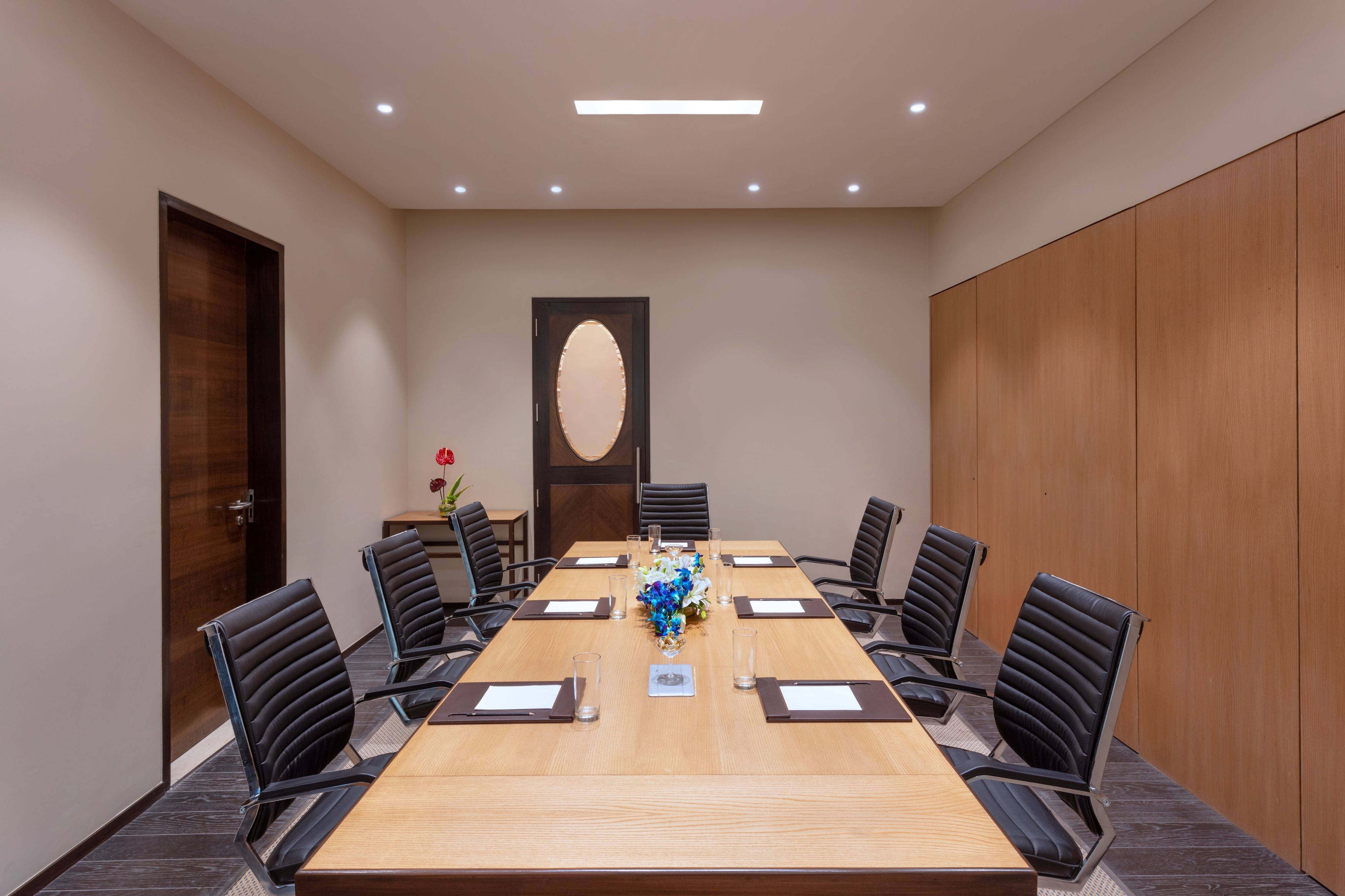 Un salón de conferencias con una larga mesa, sillas negras y un centro de mesa decorativo.