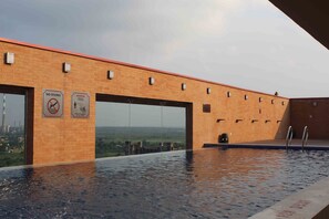 Een overloopzwembad met uitzicht op een verafgelegen stadsgezicht, een bakstenen gebouw met grote ramen en twee waarschuwingsborden aan de muur.