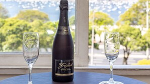 A bottle of Freixenet wine and two glasses on a table with a view of a mountain and a body of water. - Moderno Apartamento na Praia de Botafogo (Rio de Janeiro)