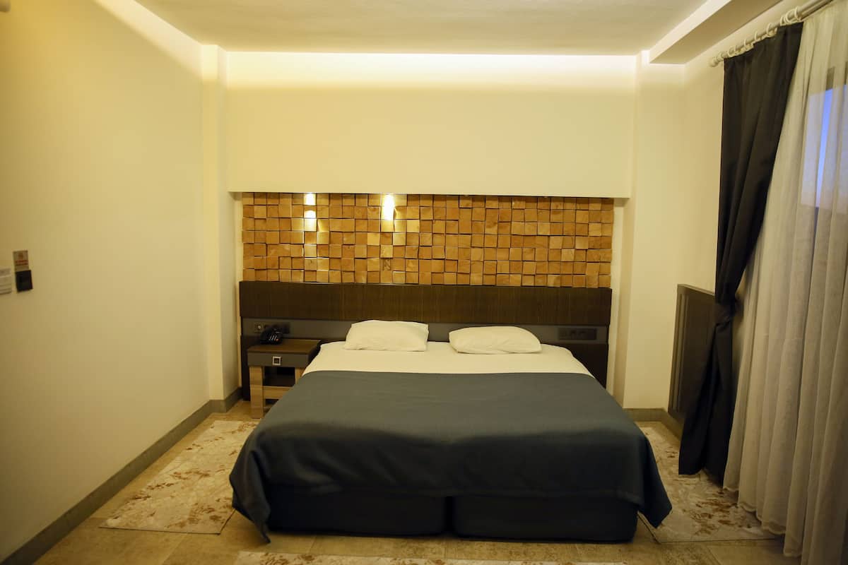 A hotel room with a bed, a nightstand, a wall-mounted TV, and a window with curtains.
