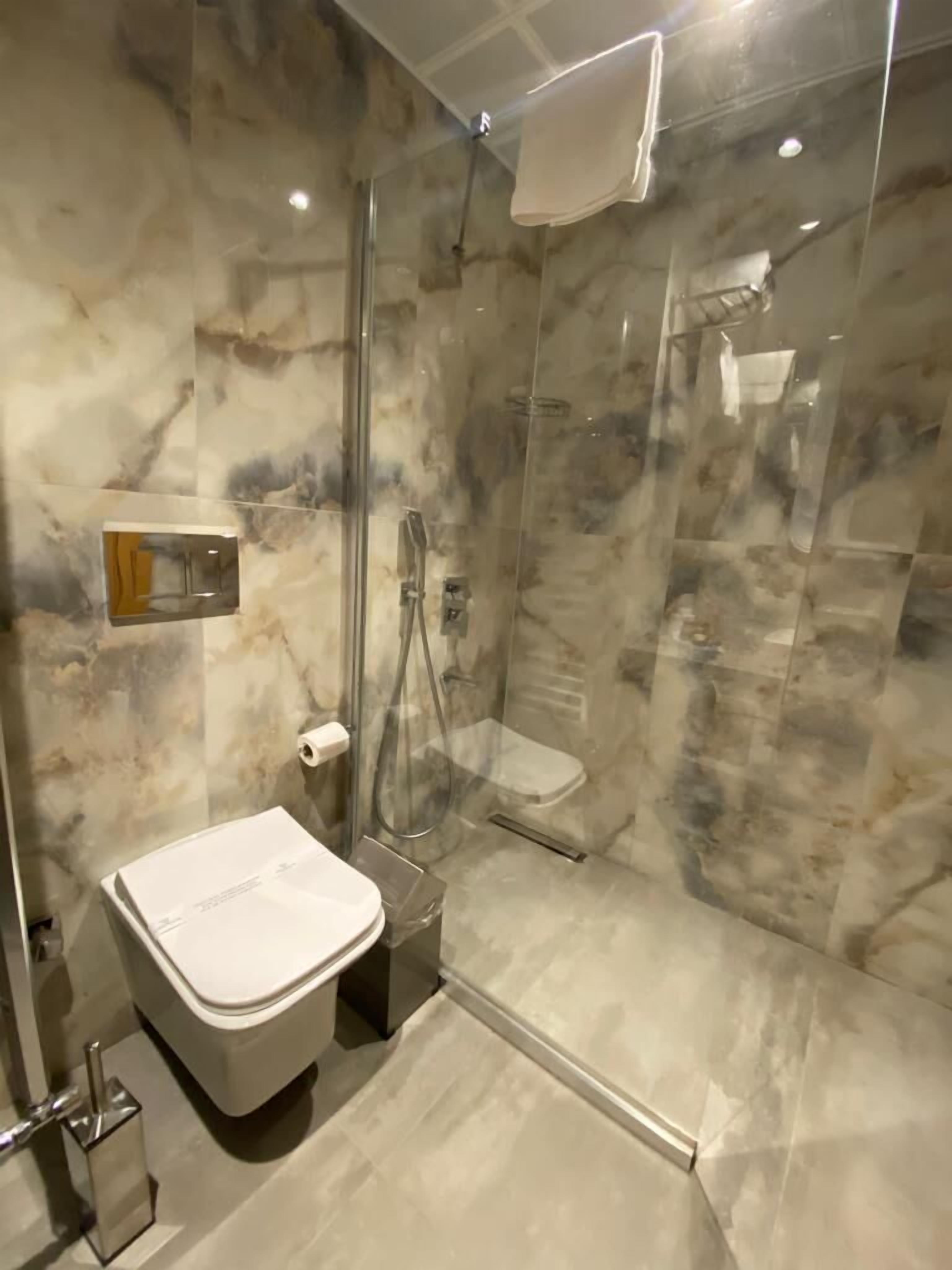 A modern bathroom with a glass-enclosed shower, a white sink, and a marble wall.