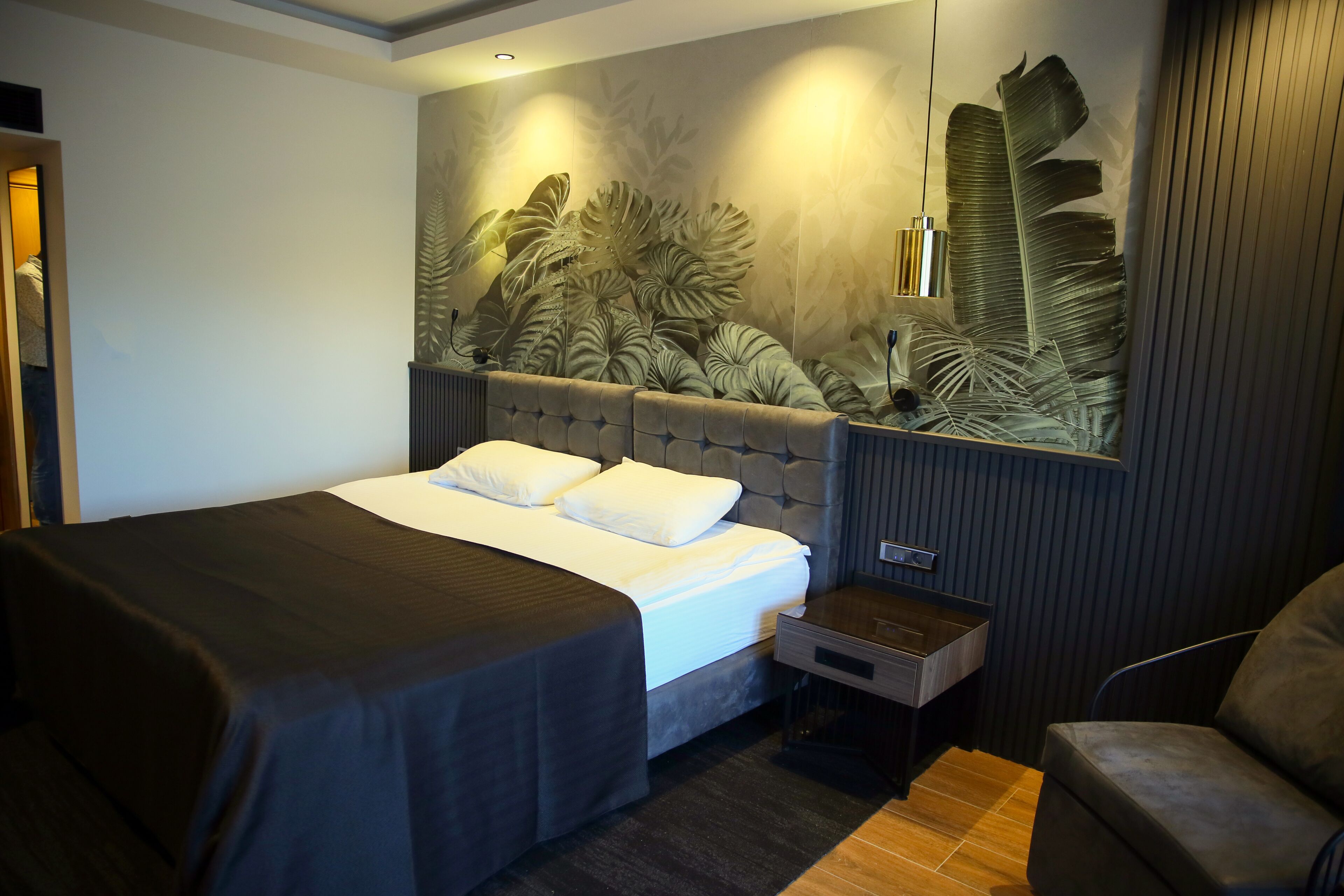 A modern hotel room with a large bed, a nightstand, a seating area, and a wall with a leaf pattern.
