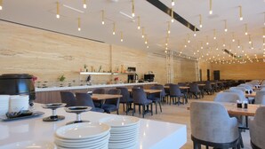 A modern restaurant with a long counter, multiple tables, and chairs. - Amorium Hotel (Kastamonu)
