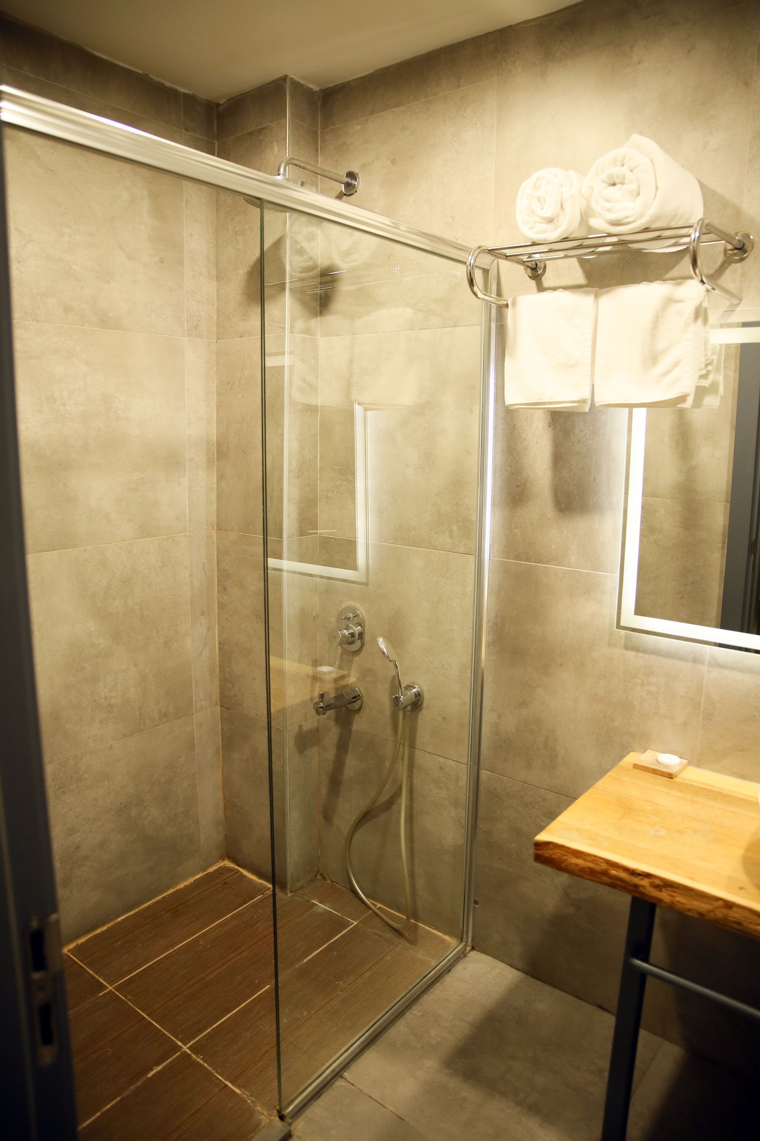 Ducha con cerramiento de vidrio, tocador de madera y toallero con toallas.