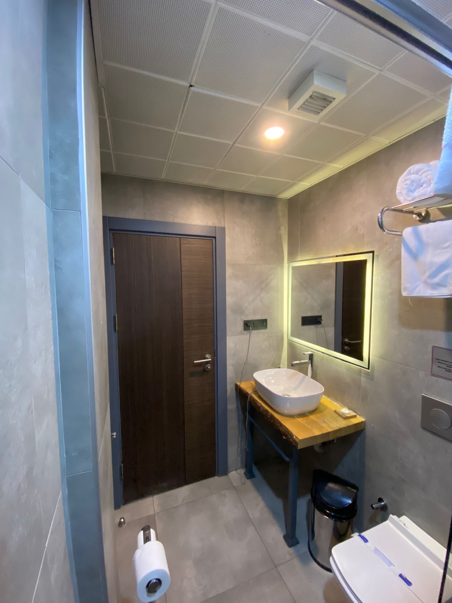 A modern bathroom with a wooden vanity, a large mirror, a white sink, and a toilet.