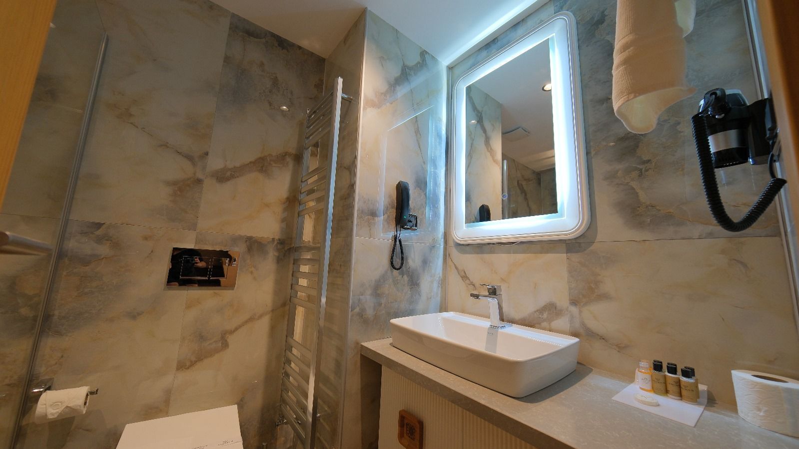 A modern bathroom with a marble wall, a glass shower enclosure, a vanity with a sink, and a mirror.