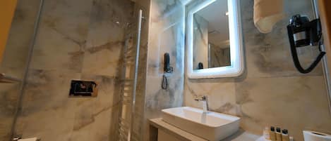 A modern bathroom with a marble wall, a glass shower enclosure, a vanity with a sink, and a mirror.