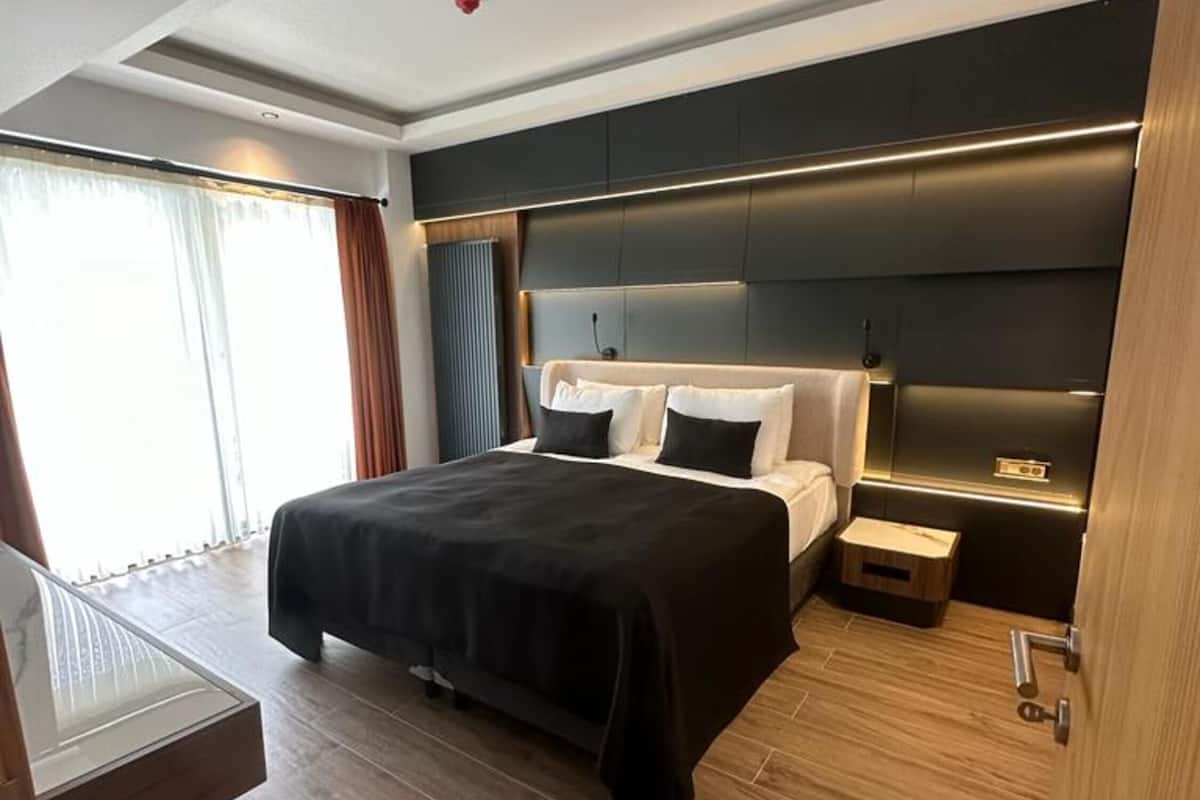 A modern hotel room with a large bed, bedside tables, a desk, and a view of the outdoors.