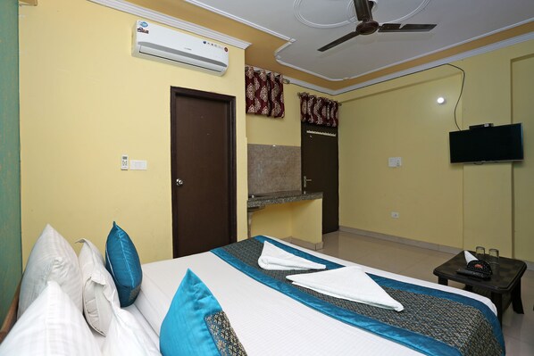A hotel room with a bed, pillows, a flat-screen TV, an air conditioner, and a ceiling fan.