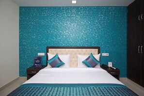 Una habitación de hotel con una cama grande, cabecera y pared texturizada color verde azulado.