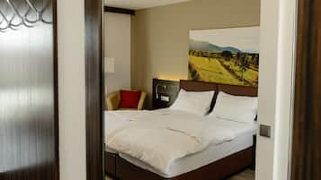 A hotel room with a large bed, a nightstand, a lamp, a red pillow, and a painting of a landscape on the wall.