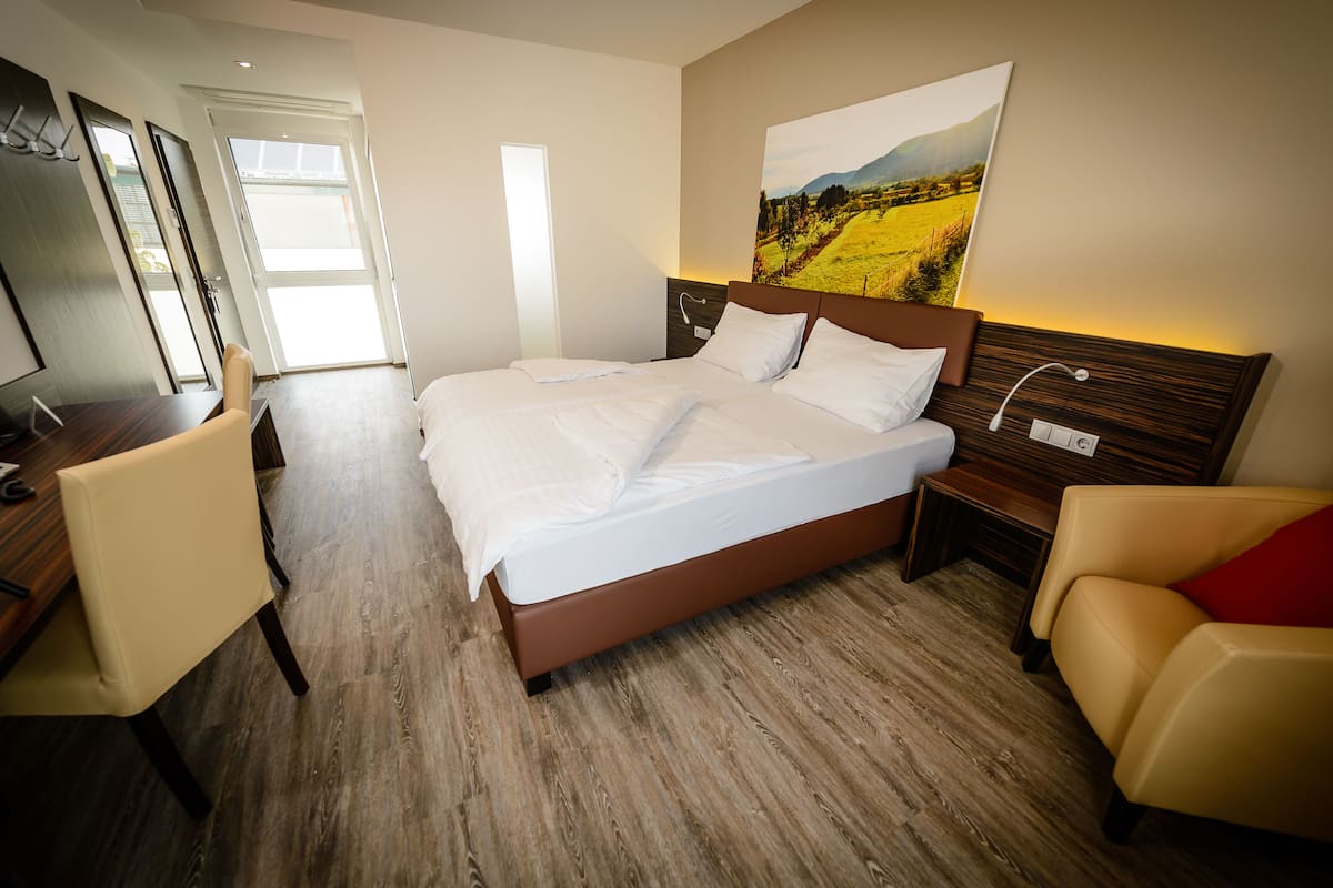 A modern hotel room with a large bed, a desk, a chair, and a painting on the wall.