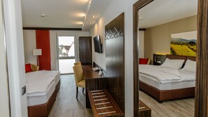 A hotel room with two beds, a desk, a chair, a TV, and a large mirror.