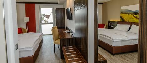 Une chambre d’hôtel avec deux lits, un bureau, une chaise, une télévision et un grand miroir.