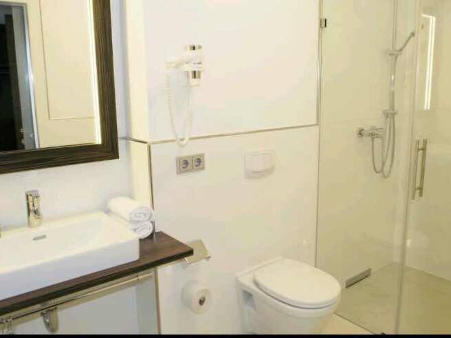 Un baño con lavamanos blanco, espejo, inodoro y ducha.