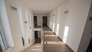 A spacious, well-lit hallway with a wooden floor, a metal railing, and a staircase leading to a second floor.