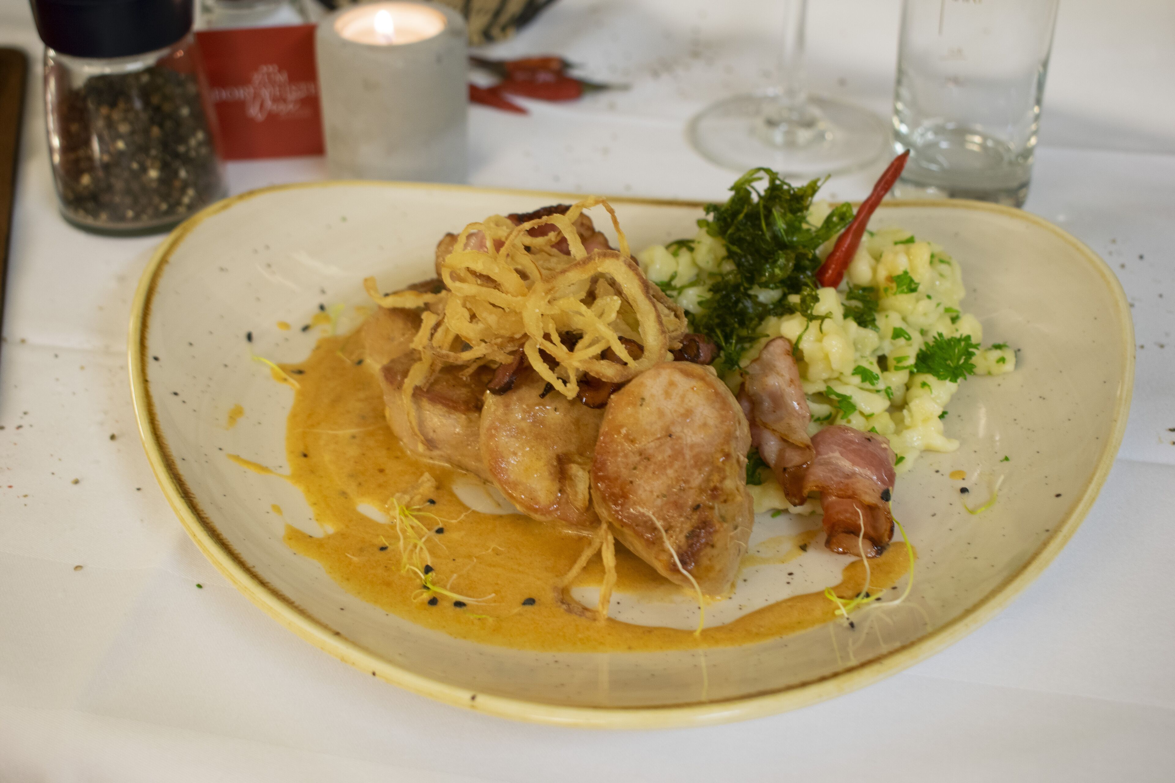 Un plato de comida con salsa cremosa, adornado con hierbas y tocino.