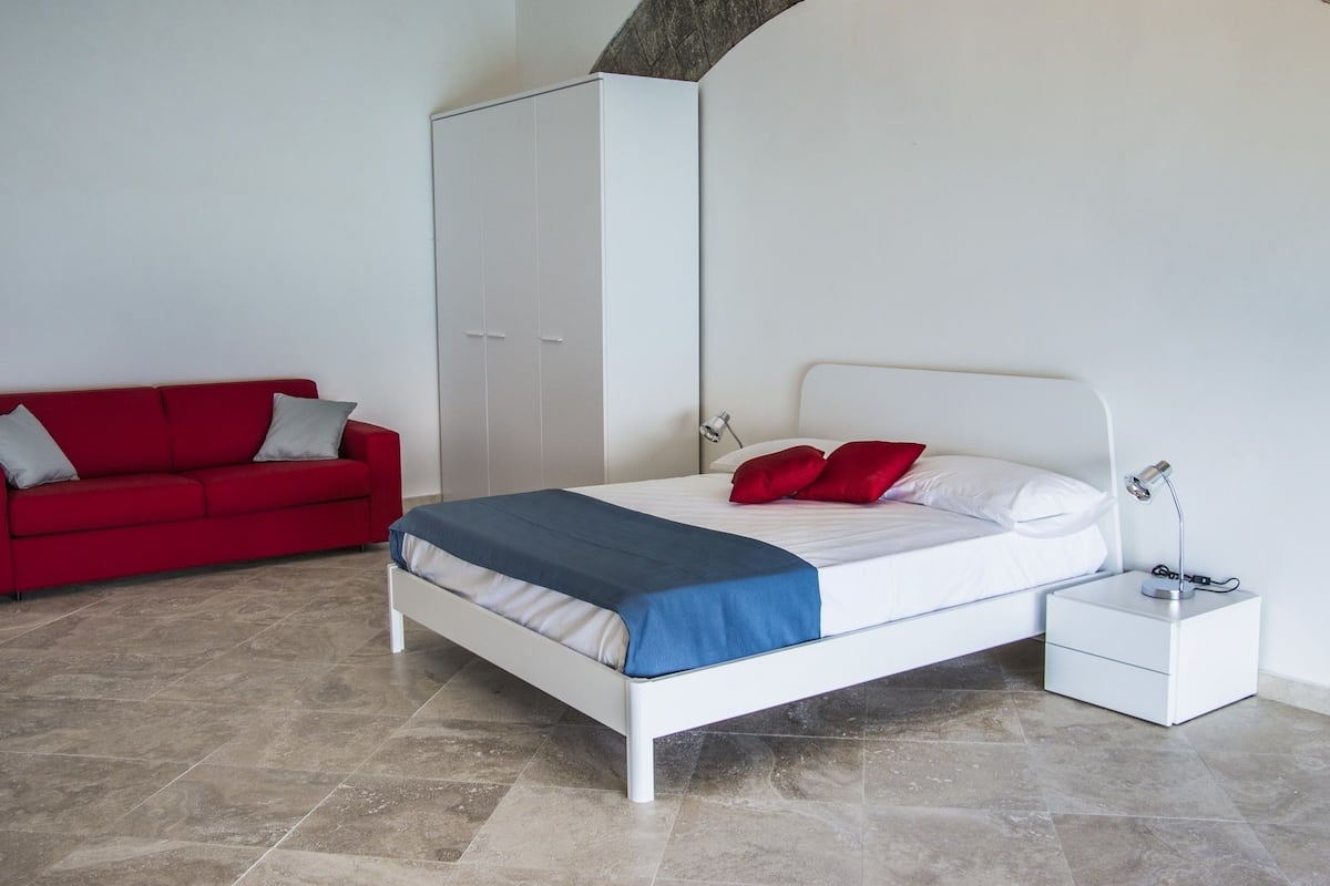 Quarto com uma cama, um sofá vermelho, um guarda-roupa e uma mesa de cabeceira com abajur.