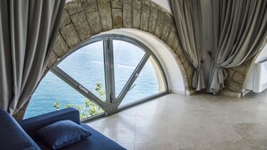 A room with a large arched window overlooking the sea, a blue sofa, and curtains. - Sunrise Guest House (Gaeta)