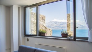 A room with a large window overlooking a coastal view, a grey sofa, and a radiator. - Sunrise Guest House (Gaeta)