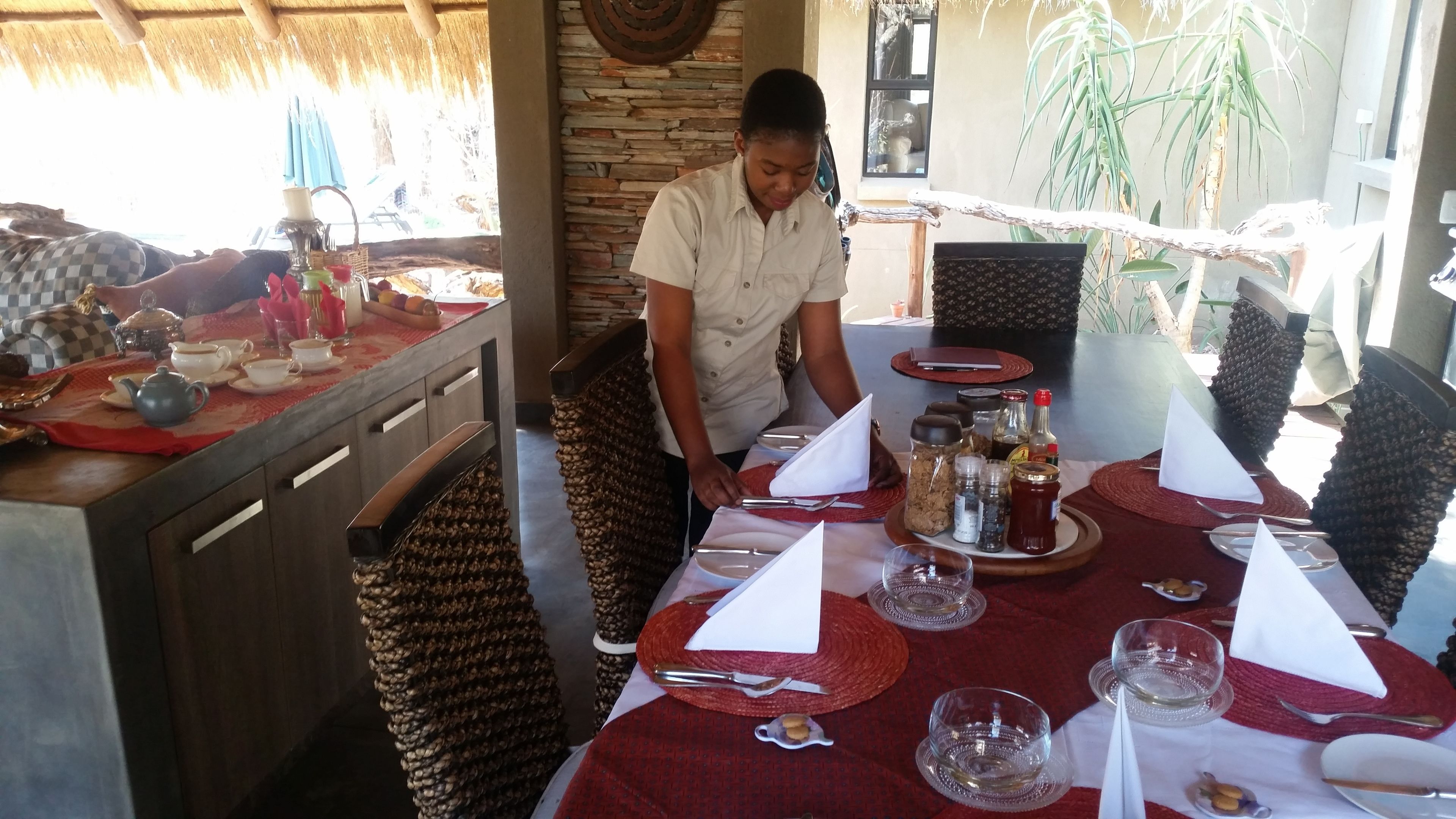 A dining area with a table set for two, featuring a red tablecloth, white napkins, and various condiments and utensils.